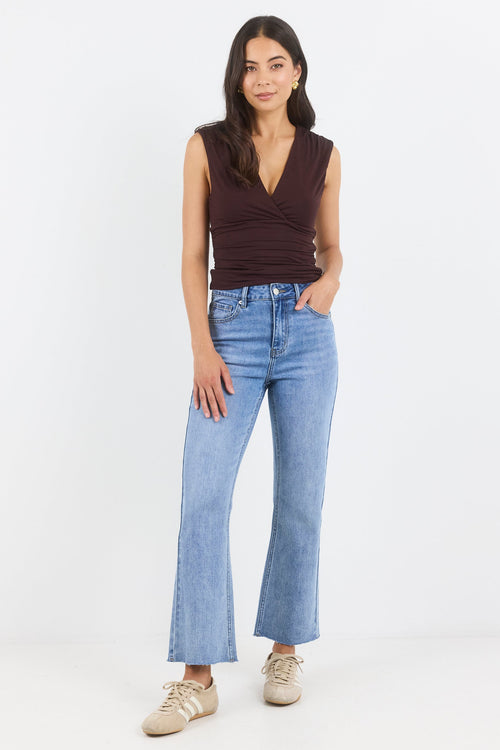 Woman wearing a brown sleeveless top and blue jeans on a white background