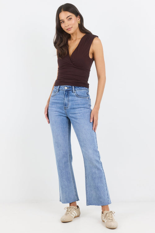 Woman wearing a brown sleeveless top and blue jeans on a white background