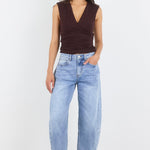 Woman wearing a brown sleeveless top and light blue jeans on a white background