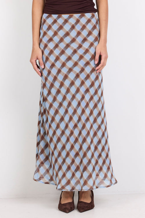 A model wearing a brown and light blue checkered maxi skirt with a dark brown top and brown pointed-toe heels, standing against a plain white background.