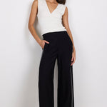 Woman wearing a white sleeveless top and black pants on a white background