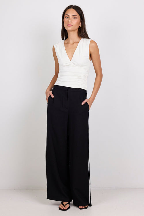 Woman wearing a white sleeveless top and black wide-leg pants on a white background