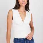 Woman wearing a white sleeveless top and blue jeans against a plain background