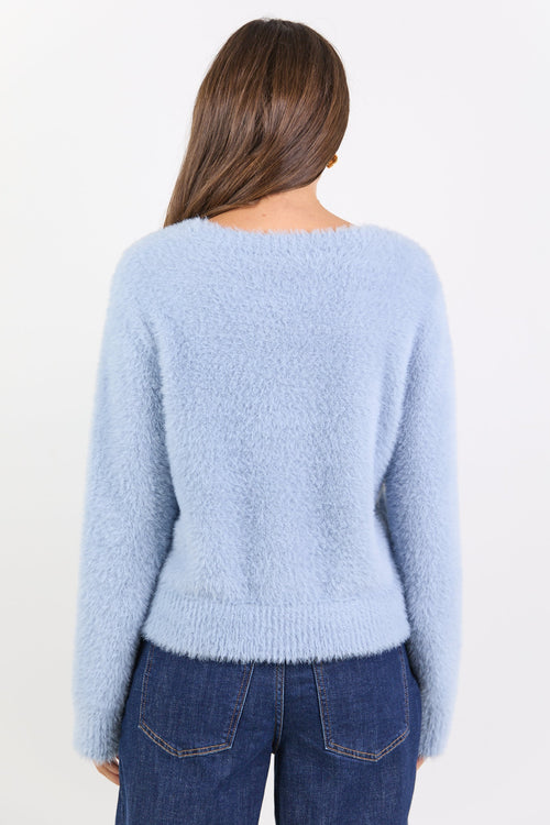 Person wearing a light blue sweater and dark blue jeans on a white background