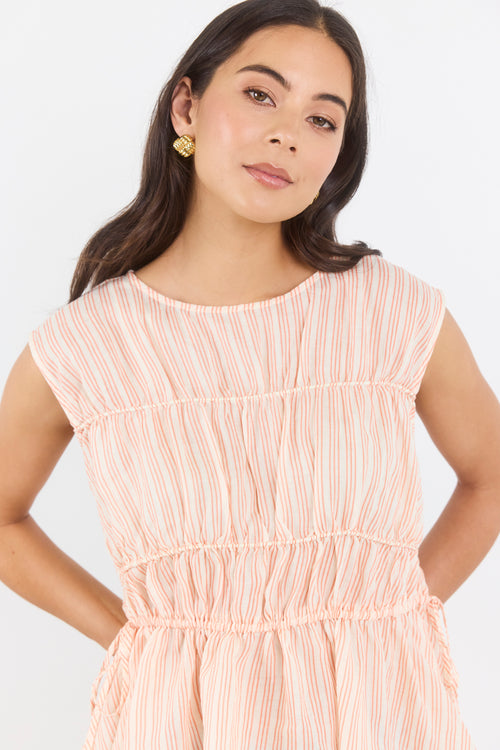 Woman wearing a peach-colored dress with thin white stripes on a white background