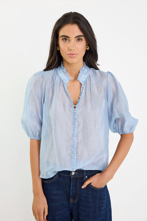Woman wearing a light blue blouse with puffed sleeves against a white background