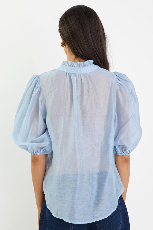 Woman wearing a light blue blouse with puffed sleeves against a white background