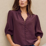 Woman standing against a beige wall with a stone wall in the foreground