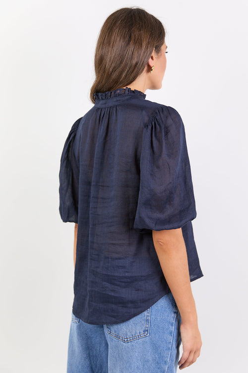 Person wearing a navy blue blouse with puffed sleeves on a white background