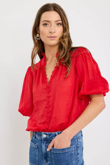 Woman wearing a red blouse with puffed sleeves and blue jeans on a white background