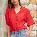 Woman wearing a red blouse and blue jeans against a stone wall.