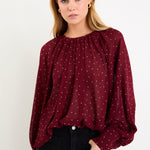 Model wearing a burgundy long sleeve polka dot blouse with a floaty fit, crew neckline and balloon sleeves.