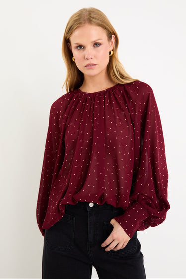 Model wearing a burgundy long sleeve polka dot blouse with a floaty fit, crew neckline and balloon sleeves.
