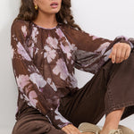 Woman wearing a floral blouse and brown pants sitting on the floor against a white background