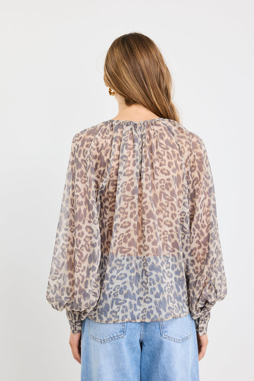 Woman wearing a leopard print blouse and light blue jeans on a white background