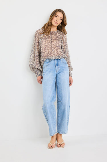 Woman wearing a patterned blouse and light blue jeans on a white background