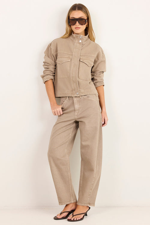 A model wearing a matching beige cropped jacket and wide-leg pants set, styled with black sunglasses and black sandals, standing against a plain white studio background.