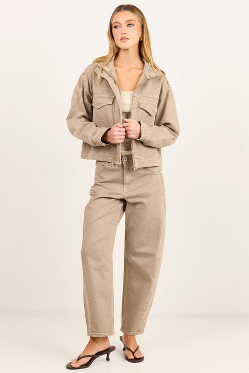 A woman modeling a matching beige cropped utility jacket and wide-leg jeans set, paired with black heeled sandals, against a plain white studio background.
