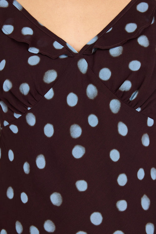 Close-up of a dark brown or very deep burgundy top with light blue polka dots, featuring a ruffled collar and shoulder details.