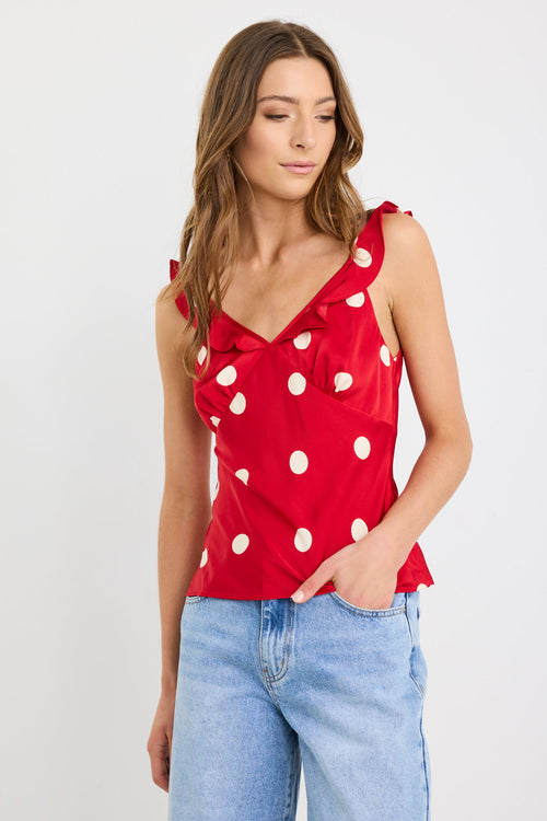 Woman wearing a cherry red polka dot cami top with ruffle neckline and tie straps, styled with light-wash wide-leg jeans.