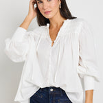 A woman wearing an ivory blouse with pintuck detailing, button-front closure, and tie neckline, styled with dark indigo mid-rise jeans.