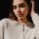Woman wearing a light gray cardigan against a dark background