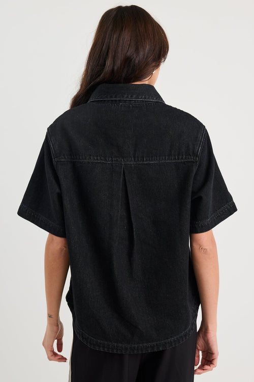 Person wearing a black denim shirt and pants on a white background