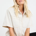 model wears an ecru denim short sleeve shirt with black pants