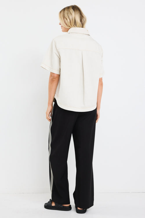 model wears an ecru denim short sleeve shirt with black pants