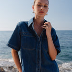 Woman wearing a denim shirt standing on a beach with ocean in the background