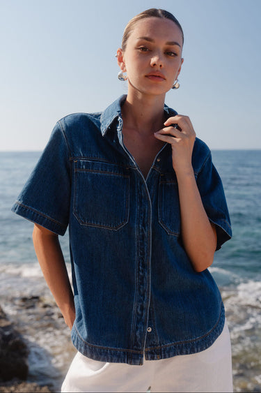 Woman wearing a denim shirt standing on a beach with ocean in the background