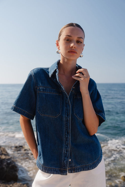 Woman wearing a denim shirt standing on a beach with ocean in the background