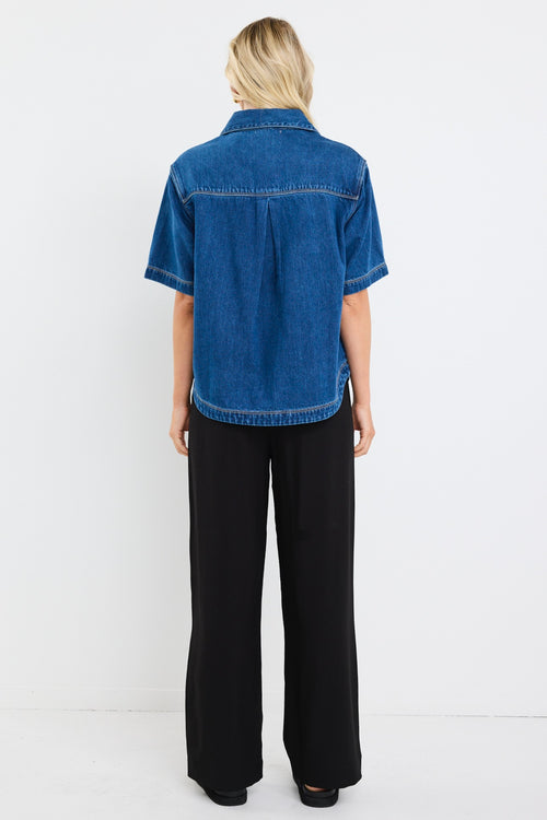 model wears a blue short sleeve denim shirt with black pants