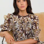 Woman wearing a patterned dress sitting on a beige chair against a white background