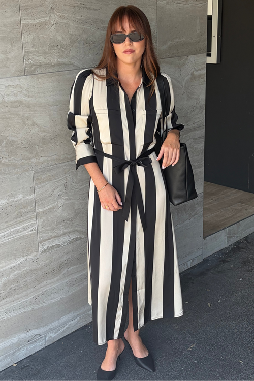 Woman wearing a black and white striped dress standing against a gray wall.
