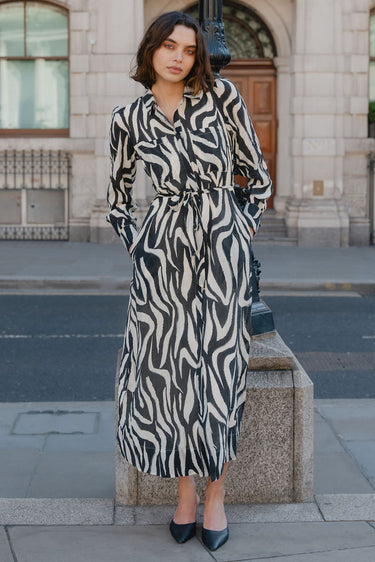 Woman in a zebra print dress standing on a street corner with a building in the background