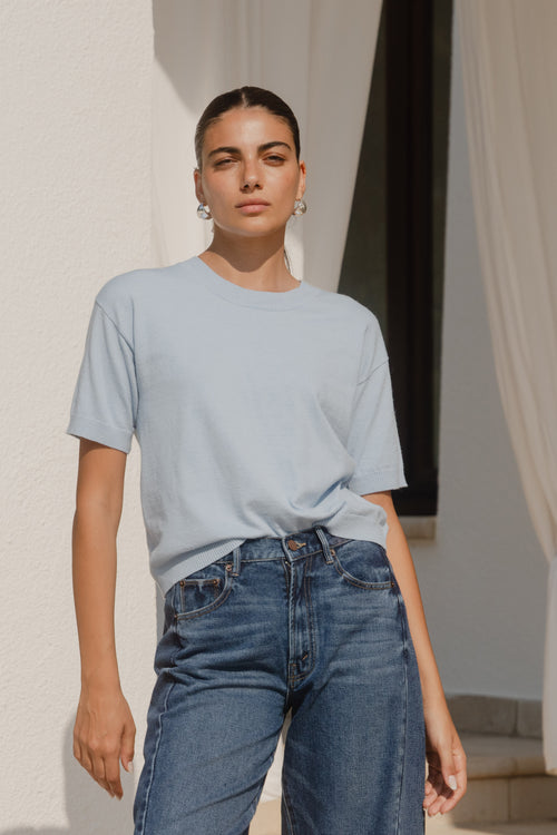 Woman wearing a light blue t-shirt and jeans standing against a neutral background