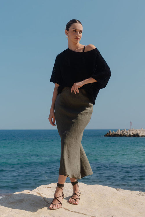 Woman standing on a rocky outcrop by the ocean with clear blue sky.