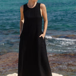 Woman in a black dress standing on a rocky shore with ocean in the background