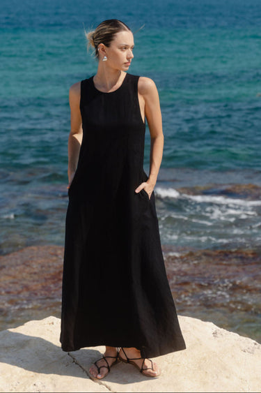 Woman in a black dress standing on a rocky shore with ocean in the background