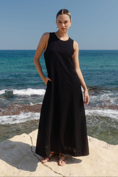Woman in a black dress standing on a rocky shore with ocean in the background