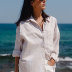 Woman in a striped shirt and sunglasses standing on a beach with ocean in the background