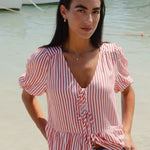 Woman in a striped shirt and jeans standing on a beach with boats in the background