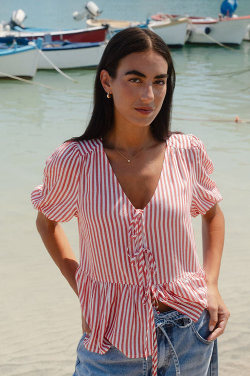 Woman in a striped shirt and jeans standing on a beach with boats in the background
