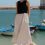 Woman standing on rocks by a harbor with boats and a clear sky