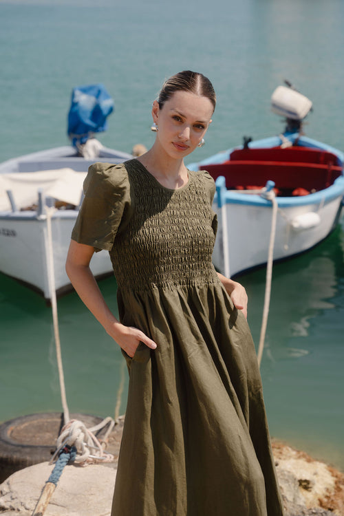 Woman in a green dress standing by a dock with boats in the background