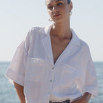 Person wearing a white shirt and blue jeans standing by the ocean.