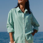 Woman wearing a green and white striped shirt and sunglasses by the ocean.