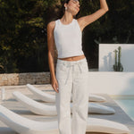 Woman in white outfit standing on a modern outdoor chair by a pool with greenery in the background