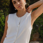 Woman wearing a white sleeveless top and blue jeans with a blurred green background